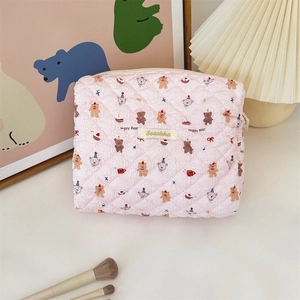 Pink quilted makeup bag with cute happy bear print and woven label on a cozy table