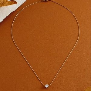 Elegant gold necklace with a round claw-set light blue zircon on a brown leather background