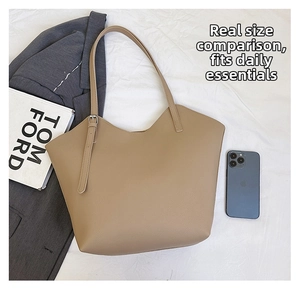 Detail view of large khaki tote bag with adjustable strap next to a phone and book