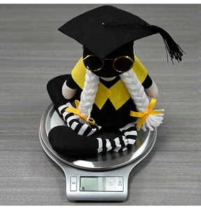 Close-up of graduation gnome with mortarboard and glasses on a scale weighing 178.4g