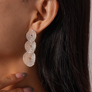 Close-up of geometric hollow mesh silver circular drop earrings worn by a model
