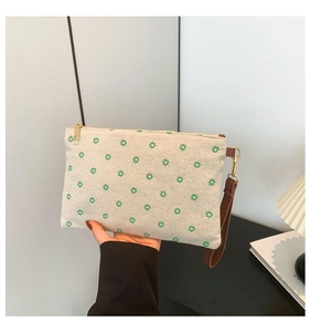 Detail of beige canvas envelope clutch with green floral print and brown wrist strap