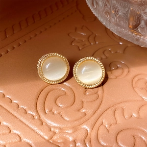 Macro view of round cat-eye stone earrings with vintage gold woven metal border details