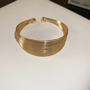 Detail view of a minimalist multi-layered gold metal open cuff bracelet on white background