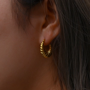Macro detail of the glossy gold-plated croissant hoop earring with spiral texture