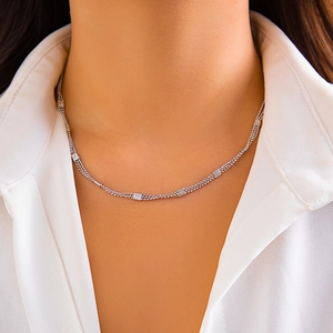 Macro shot of layered silver bead chains with square geometric accents on a white shirt