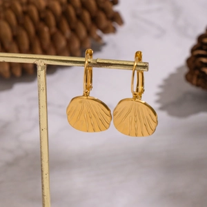 Golden fan-shaped textured leaf earrings on stand with natural pine cones on marble