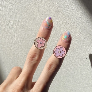 Floral daisy enamel rings in pink and purple colors worn on fingers with colorful nail art