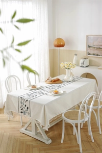 Close-up of geometric floral embroidery and fringe details on a beige linen tablecloth