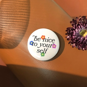 Detail of white tinplate badge with 'be nice to yourself' text and floral patterns