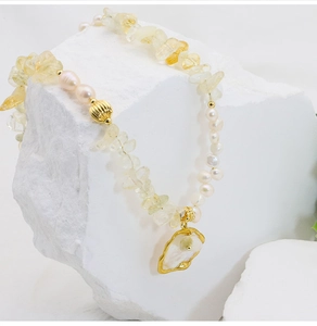 Close-up of Baroque pearls and citrine stone necklace on white textured stone base