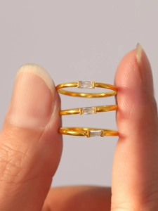 Macro shot of three stacked gold rings featuring rectangular zircon stones held by fingers