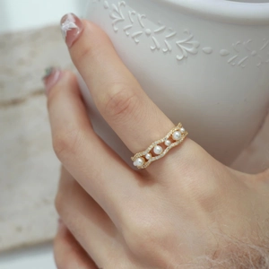 Detail showing wavy gold pearl ring with diamonds on hand by a white ceramic cup