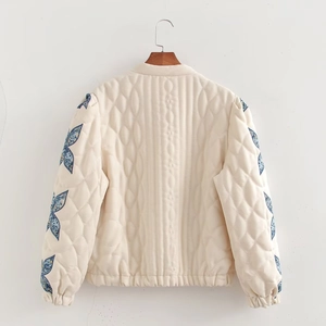 Detail of beige quilted jacket featuring intricate blue floral embroidery on sleeves