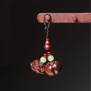 Macro shot of hand-carved sandalwood persimmon and lotus pod charm on woven cord