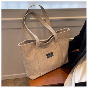Detail of oat-beige canvas tote bag showing tight fabric texture and front fashion patch