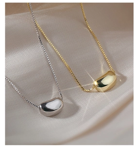 Close-up of a minimalist golden bean pendant on a fine box chain over beige silk fabric