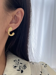Close-up of golden irregular C-shaped earring with polished finish on a model's ear