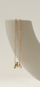 Gold stainless steel necklace with emerald green zircon triple-ring pendant on ceramic