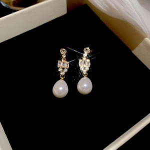 Macro shot of gold plated earrings featuring zircon stones and a drop pearl on black velvet