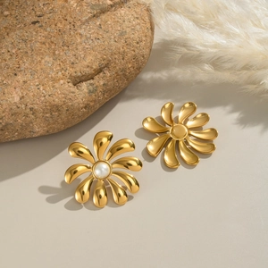 Macro detail of 18K gold plated flower earrings with pearl on a textured stone surface
