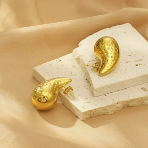 Detailed view of gold chunky teardrop earrings with hammered texture on white stone