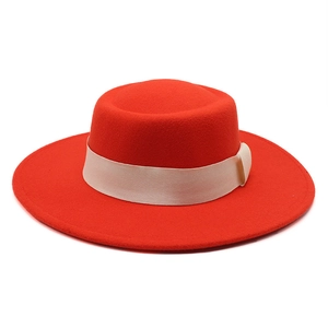 Detail of red wool felt boater hat with a cream satin ribbon on plain white background