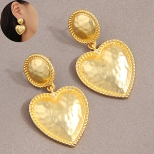 Elegant gold heart earrings with hammered texture finish on a soft grey fabric backdrop