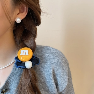 Détail d'un chouchou en tissu bleu marine avec pendentif 'm' jaune et une perle blanche