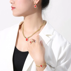 Detail view of gold jewelry set with red teardrop pendants worn by a model in a white suit