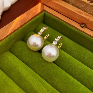 Macro view of gold pearl earrings with sparkling rhinestones in a green velvet jewelry box