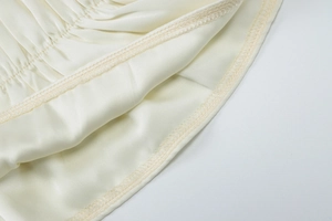 Detailed close-up of high-quality edge stitching on a beige chiffon pleated dress