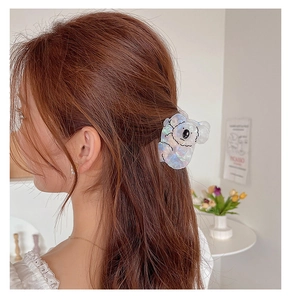 Close-up of a cute iridescent koala hair claw clip worn on a woman's brown hair