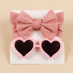 Close-up of pink ribbed bow headband and heart-shaped sunglasses set on card