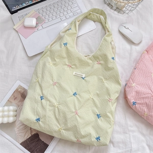 Detail of light green quilted tote bag with colorful bow embroidery on a bed