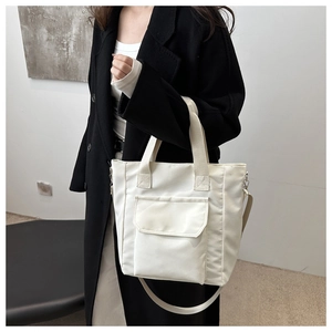 Detailed view of a white casual tote bag with a front pocket on a black coat model