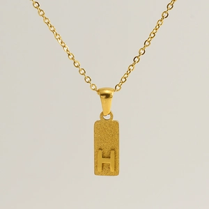Close-up of a gold rectangle pendant with a 3D embossed letter H and frosted texture