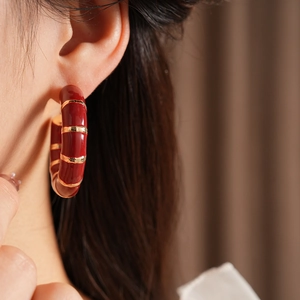 Close-up of vintage red enamel C-shape hoop earring with gold stripes on model