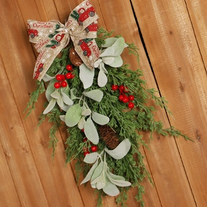 Christmas teardrop swag with pine cones, red berries and Merry Christmas ribbon on wood