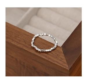 Macro detail of geometric silver bead ring with square and round charms on wooden box