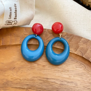Detail of red and blue color-block resin earrings with gold link on a wooden tray