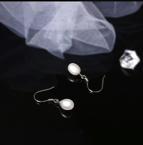 Macro shot of S925 silver hook earrings with white teardrop freshwater pearls on black surface
