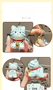 Detail of hand-carved blue resin cat keychain with a golden bell and lucky charm