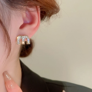 Close-up of golden letter m earrings with zircon stones on female ear model