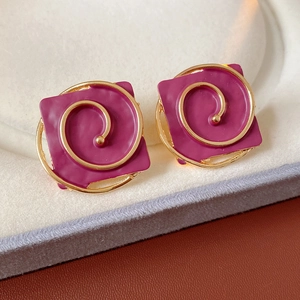 Detail of vintage square magenta enamel earrings with golden spiral patterns in a box