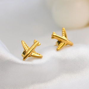 Minimalist airplane stud earrings in gold titanium steel on white silk background