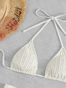 Detail of white textured bikini top with adjustable halter ties on a stone background