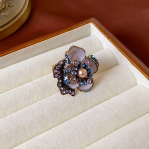 Detailed close-up of a floral ring with purple gems and a pearl in a velvet box