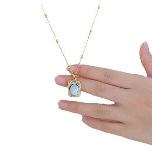 Handheld view of a gold rose pendant necklace with blue embossed gemstone detail
