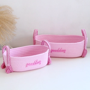 Detail of two pink cotton rope storage baskets with tassels and goodday embroidery